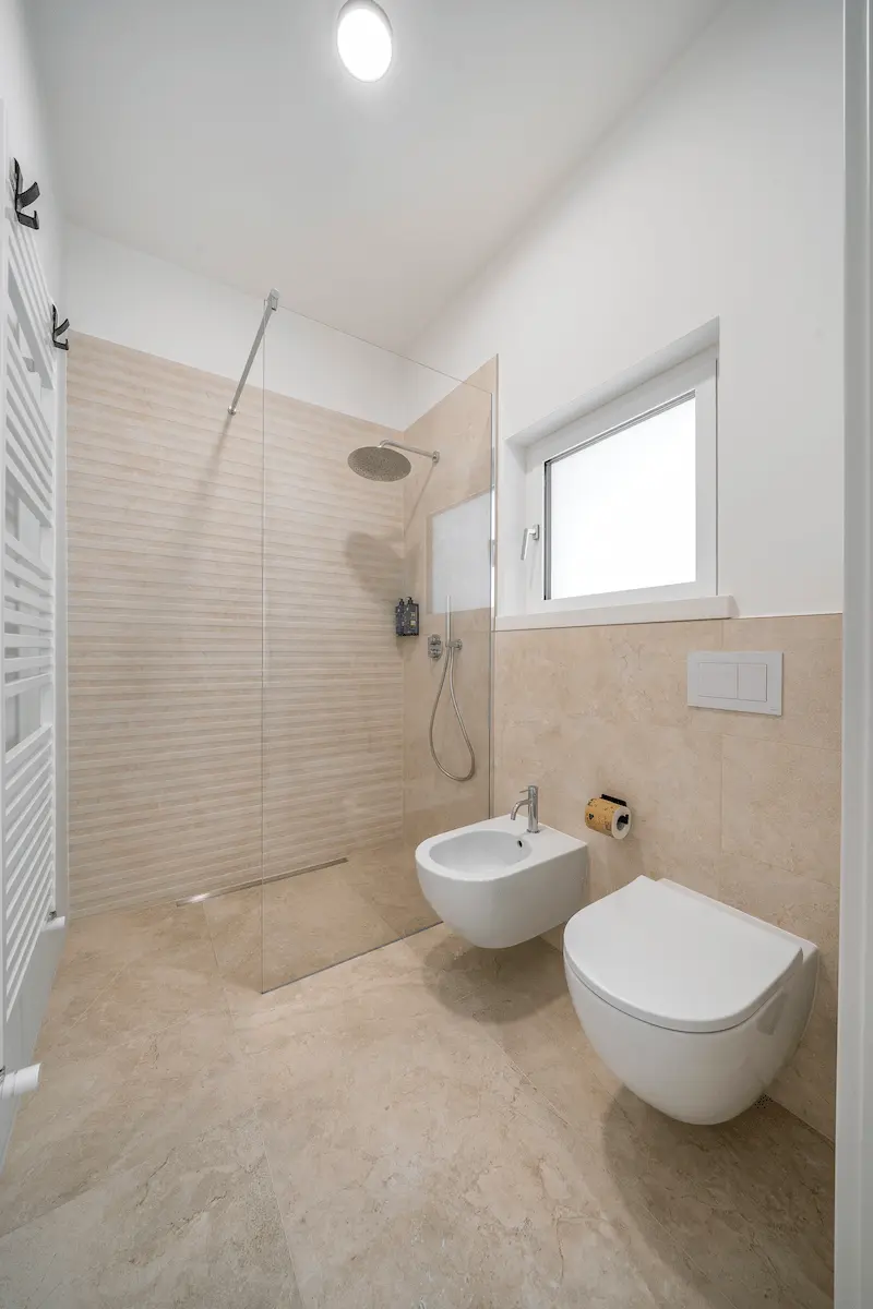 Bagno elegante con doccia e sanitari sospesi, finiture beige in camera moderna sul Lago di Garda.
