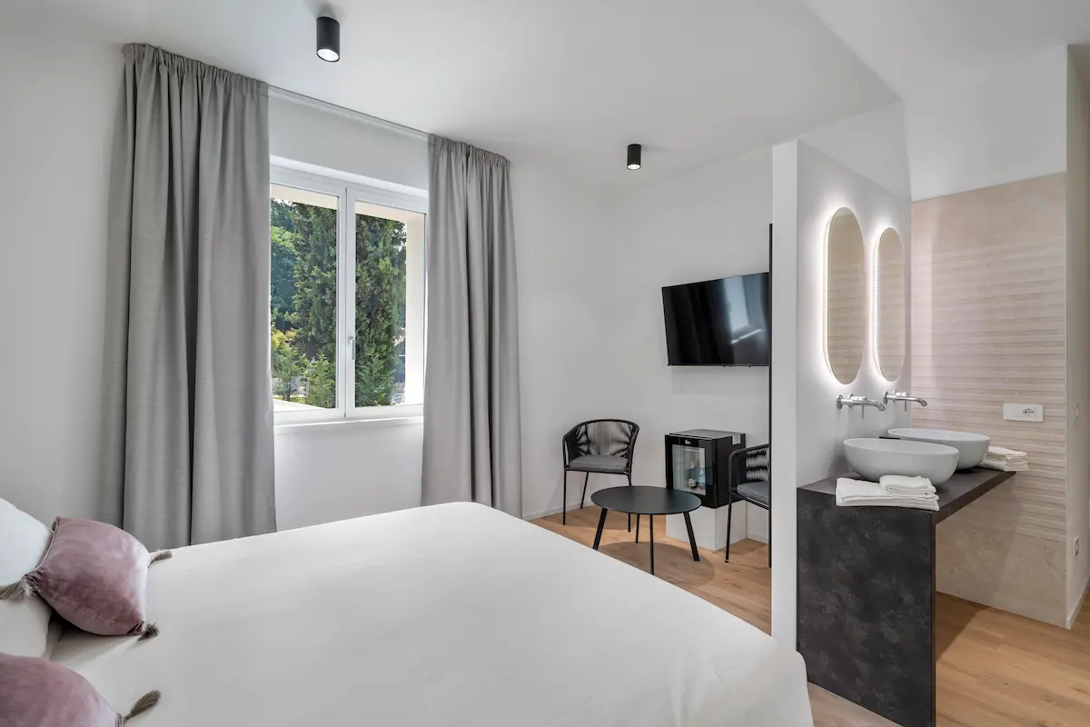 Camera con letto blu, salottino, tavolo e finestra con vista sul verde in hotel design sul Lago di Garda.