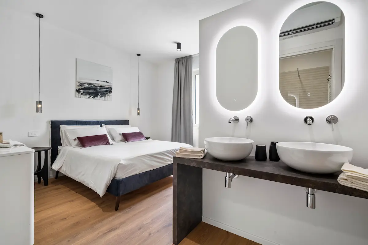 Camera moderna al The View Lake Garda con doppi lavabi, specchi retroilluminati e letto matrimoniale sullo sfondo.