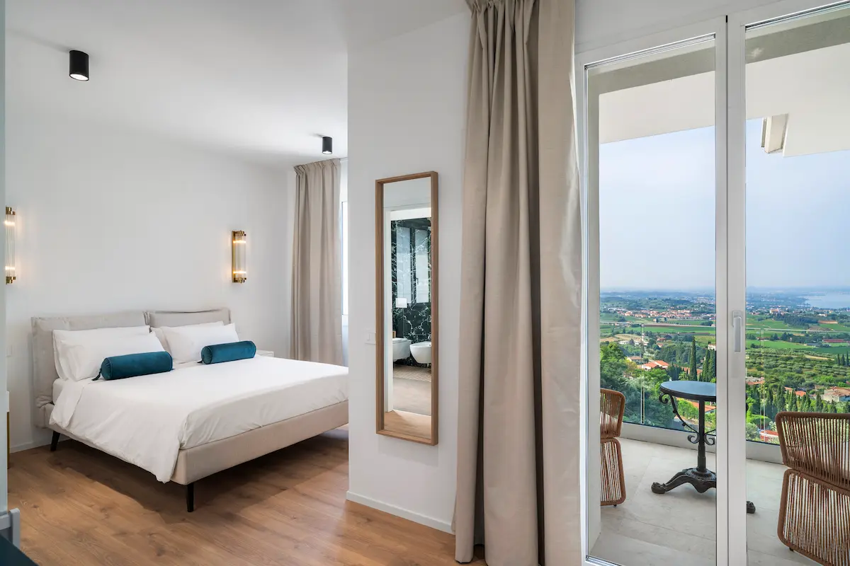 Camera con letto matrimoniale e accesso al balconcino privato vista Lago di Garda al The View, interni chiari e ariosi.