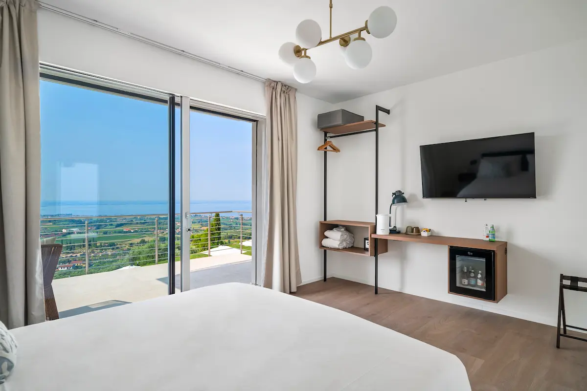 Camera con terrazzo privato e vista mozzafiato sul Lago di Garda; interni luminosi e colori blu intensi.